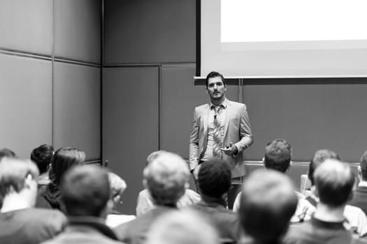 Speaker giving a talk in conference hall at business meeting event. Rear view of unrecognizable people in audience at the conference hall. Business and entrepreneurship concept.