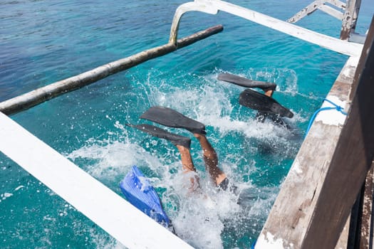 Scuba divers doing back flip into blue transparent sea from a boat's board. There are several ways to get off the boat when diving. One of them is by back roll.