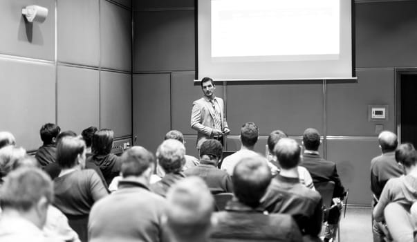 Speaker giving a talk in conference hall at business meeting event. Rear view of unrecognizable people in audience at the conference hall. Business and entrepreneurship concept.