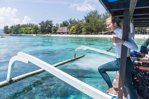 Beautiful female solo traveler relaxing and enjoying beautiful blue sea on traditional wooden boat after scuba diving trip at Gili Islands near Bali, Indonesia. Vacation and travel concept.