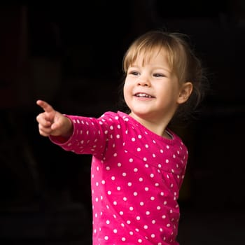 The cute little girl is showing something with her finger on black background.