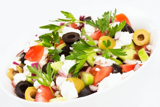 Colorful fresh Greek salad is in white dish on white background.