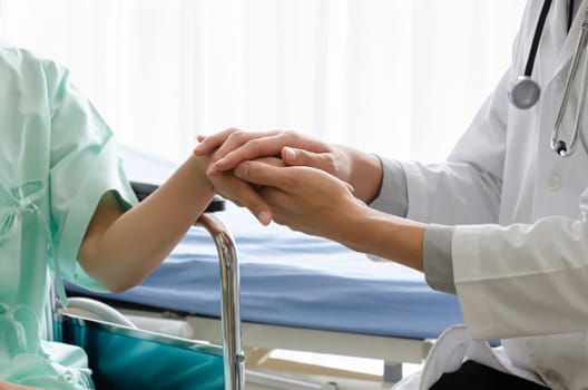 Doctor talking and consoling with holding patient hand. Encouraged to fight through disease. Female patient sitting on wheelchair in hospital ward. Healthcare and insurance concept
