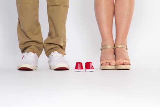 Two pairs of feet from the parents and shoes from an unborn baby, studio