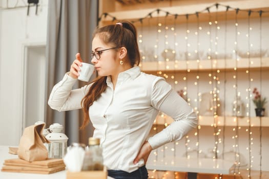 Young caucasian female entrepreneur drinking coffee and has a break. Side accidental view