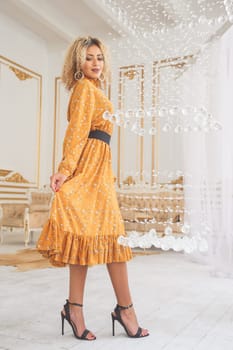 Beautiful african mixed young woman in fashionable dress and heels posing near crystal chandelier in interior.