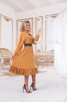 Beautiful african mixed young woman in fashionable dress and heels posing near crystal chandelier in luxury interior.