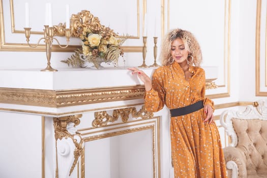Portrait of a young gorgeous african woman in summer dress, standing in a luxury interior near chimney portal fireplace.