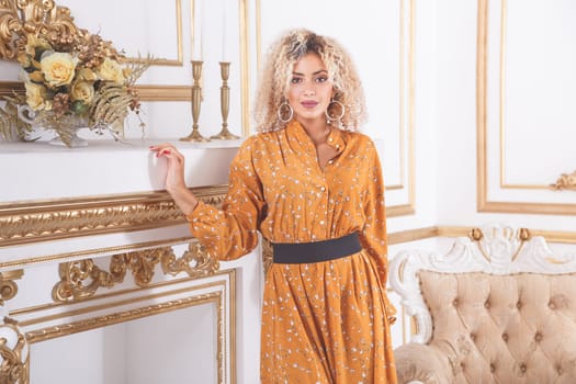 Portrait of a young gorgeous african woman in summer dress, standing in a luxury interior near chimney portal fireplace.