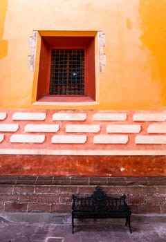 Chair against a colorful wall, with an old window with bars in the streets of San Miguel de Allende, Guanajuato, Mexico
