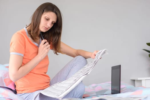 A girl is looking for work looking through ads in the newspaper, next to a laptop