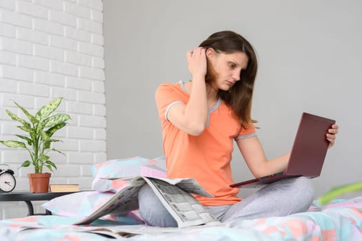Girl sitting on the bed and laying a laptop on the bed looking through ads on a laptop screen
