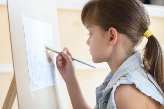 eight-year-old girl draws a brush pattern on an easel