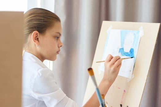A girl in light clothes sits in front of an easel and draws still life