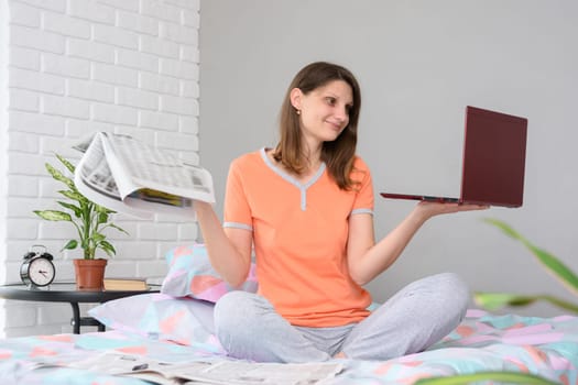 Girl holds newspapers and laptop in her hands, look at laptop
