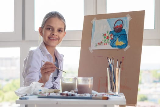 Smiling girl sits at work in the studio with a brush in her hands