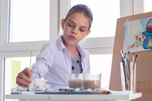 Girl-artist concentrated wets brush in paint for drawing still life