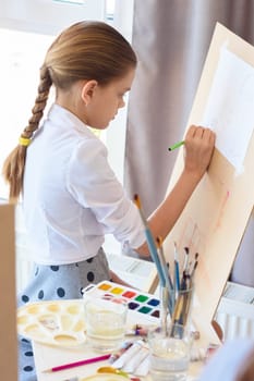 Girl is focused on drawing with a pencil on an easel