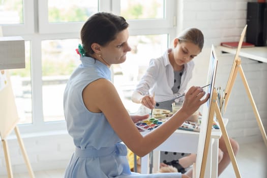 Concentrated girl draws on easel next to a young girl