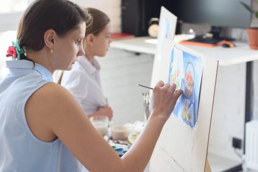 Girl sits next to the child and paints still life