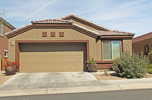 :  New one-story ranch tan and burnt orange stucco home in Tucson, Arizona, USA with beautiful blue sky and landscaping.