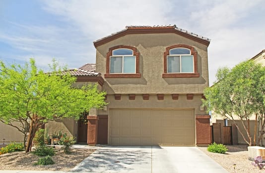 New two-story, tan and burnt orange stucco home in Tucson, Arizona, USA with beautiful blue sky and landscaping.