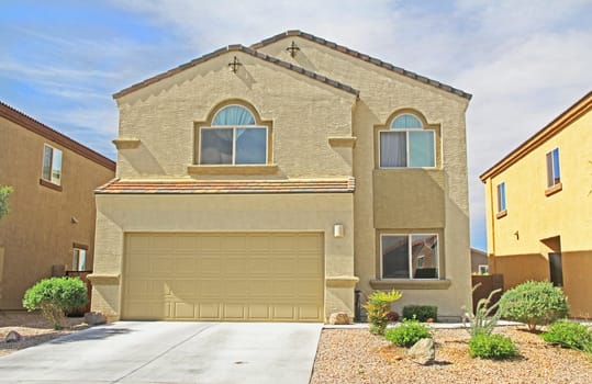 New two-story, tan and yellow stucco home in Tucson, Arizona, USA with beautiful blue sky and landscaping.