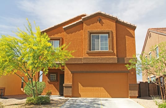 New two-story, brown and burnt orange stucco home in Tucson, Arizona, USA with beautiful blue sky and landscaping.
