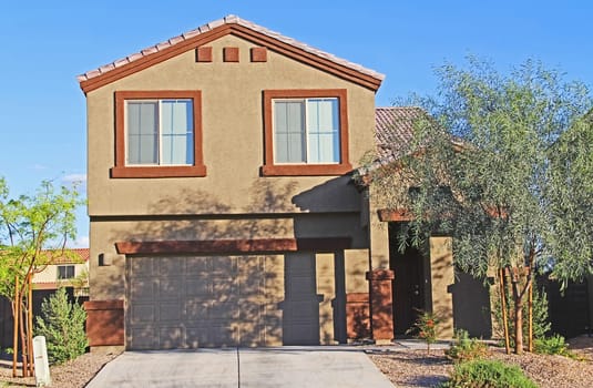 New two-story tan and burnt orange stucco home in Tucson, Arizona, USA with beautiful blue sky and landscaping.