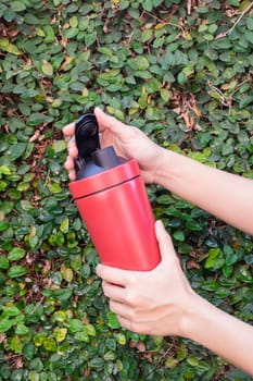 Aluminum thermos mug on hand with green leaves wall, stock photo