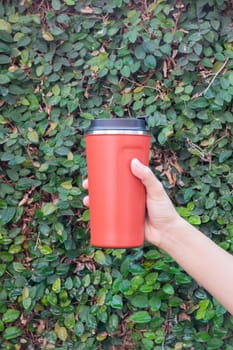 Aluminum thermos mug on hand with green leaves wall, stock photo
