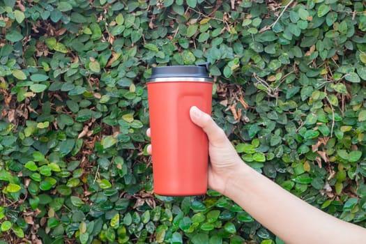 Aluminum thermos mug on hand with green leaves wall, stock photo