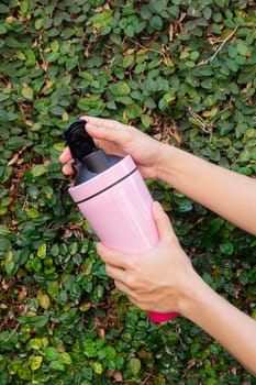 Aluminum thermos mug on hand with green leaves wall, stock photo
