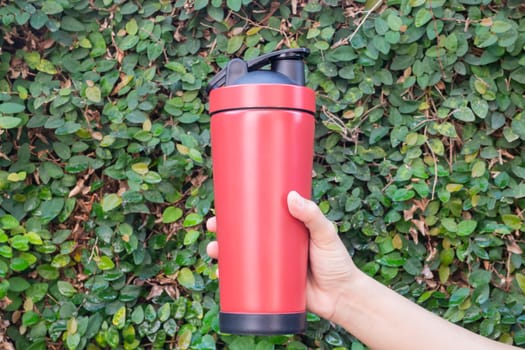 Aluminum thermos mug on hand with green leaves wall, stock photo