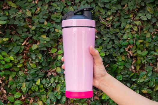Aluminum thermos mug on hand with green leaves wall, stock photo