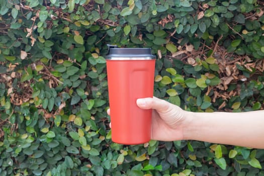 Aluminum thermos mug on hand with green leaves wall, stock photo