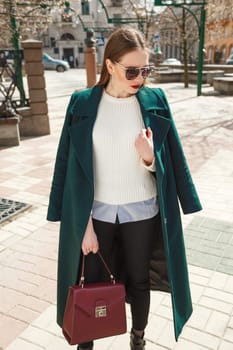 Beautiful young woman in green coat walking on the street.
