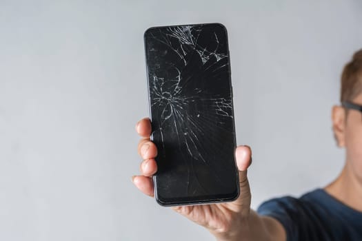 Woman holding a broken touch screen of smart phone on grey background.