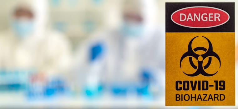 Panoramic Caution danger Signage of COVID-19 coronavirus in front of Laboratory room with background of Scientists working and researching vaccine for ncov-19 virus for world pandemic situation.
