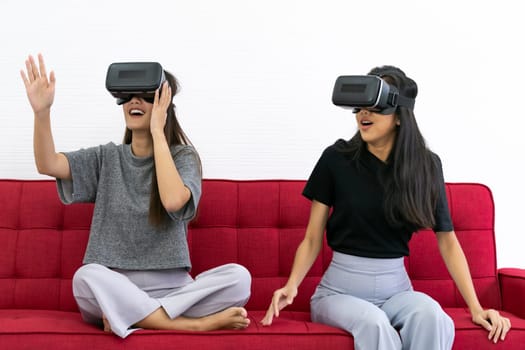 Two Asian beautiful women smiling during playing VR video games experience in living room house for good mental health while quarantine. Game technology leisure and mental health concept.