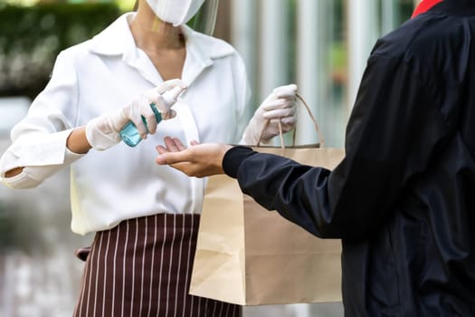 Waitress spraying alocohol on hand of deliverly man before give bakery grocery bag for cleaning and hygiene as new normal for Food deliverly service while coronavirus covid-19 pandemic.