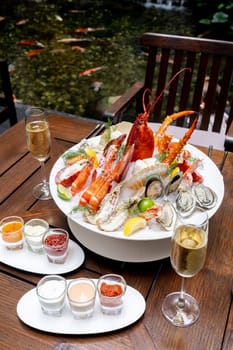 Bowl of gourmet fresh seafood on ice with savory sauce serve with white wine glass on vintage wooden table. Restaurant gastronomy food and drink consumerism concept.