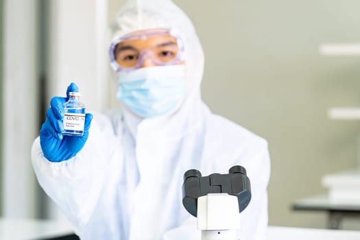 Scientist hold vaccine to immune coronavirus covid-19 pandemic in science lab. Scientist wear PPE personal protective suits  and medical goggles. Medical Science technology and healthcare concept.