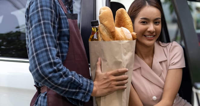 Delivery staff giving grocery bag set to asian customer woman at drive thru service station of Supermarket. Drive thru is popular service and new normal after coronavirus covid-19 pandemic.