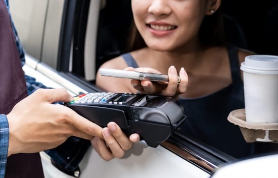 Asian woman customer make mobile payment contactless technology to waiter in drive thru food service while pickup coffee and bakery. Drive through is more  popular after coronavirus covid-19 pandemic.