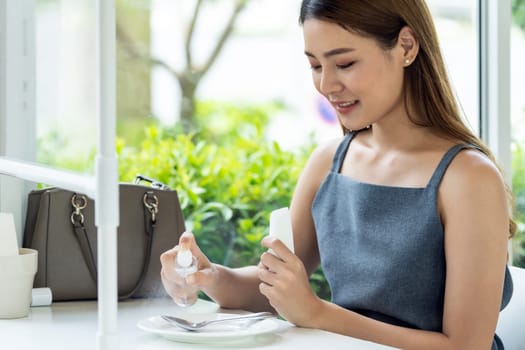 Asian attractive woman spraying alcohol on dishware in restaurant to cleaning reduce infection of coronavirus covid-19. New normal lifestyle at restauranr concept.