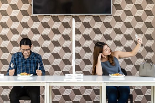 Asian couple take a selfie photo together in new normal social distance restaurant with table shiled partition to reduce infection of coronavirus covid-19 pandemic. Restaurant new normal lifestyle.
