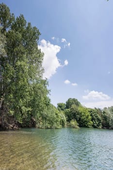 clear water and tall trees on green shore of lake in dimissed pit at urban park, shot in bright sunny light at Milan, Lombardy, Italy.