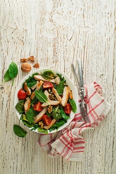 Healthy green salad with chicken breast, tomato and nuts on wooden table