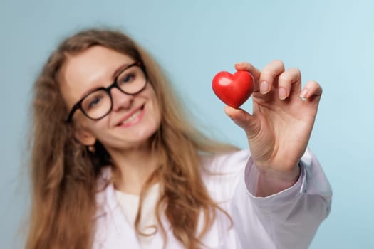 Smiling female doctor holding a red heart, symbolizing cardiology, healthcare, heart health, and medical care on a light blue background.